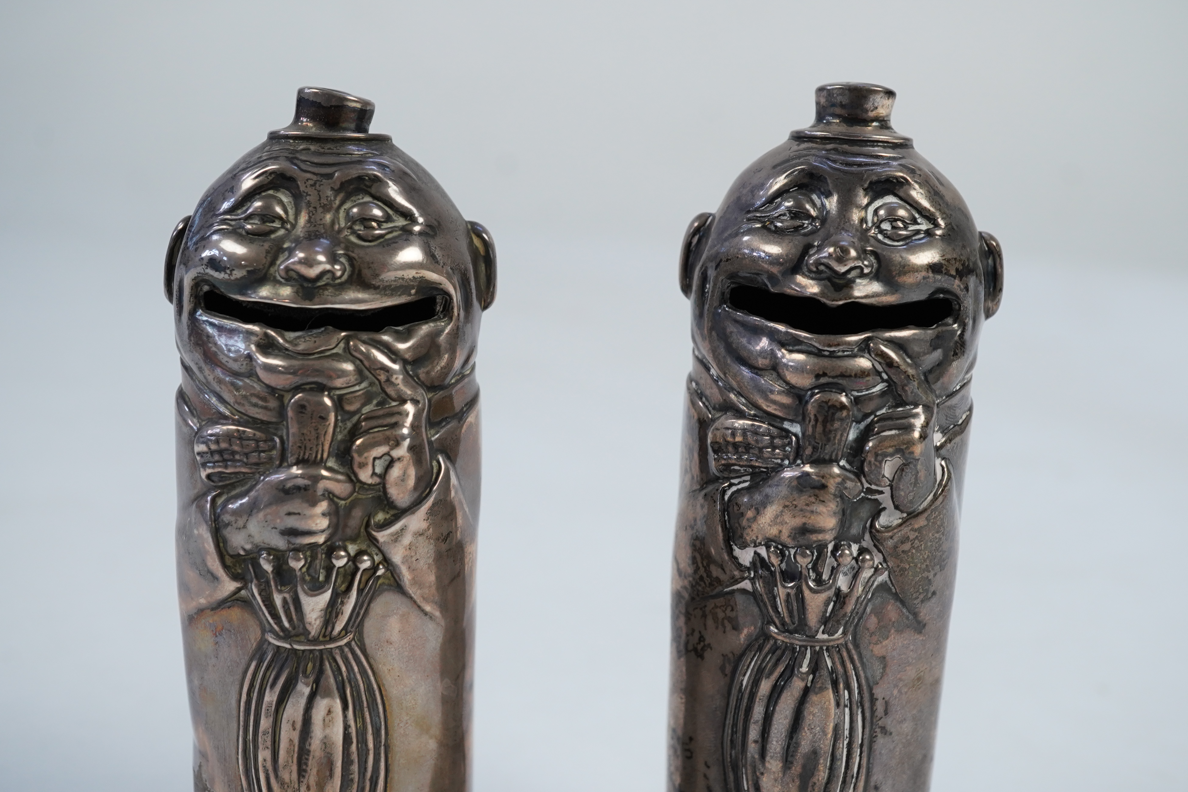 A matched pair of George V novelty silver money boxes, each cylindrical box embossed as a banker with an umbrella, the circular base inscribed 'Always be prepared for a rainy day'